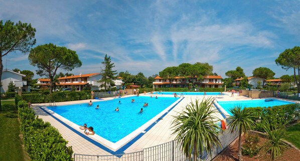 A large outdoor swimming pool surrounded by lush greenery and residential buildings.