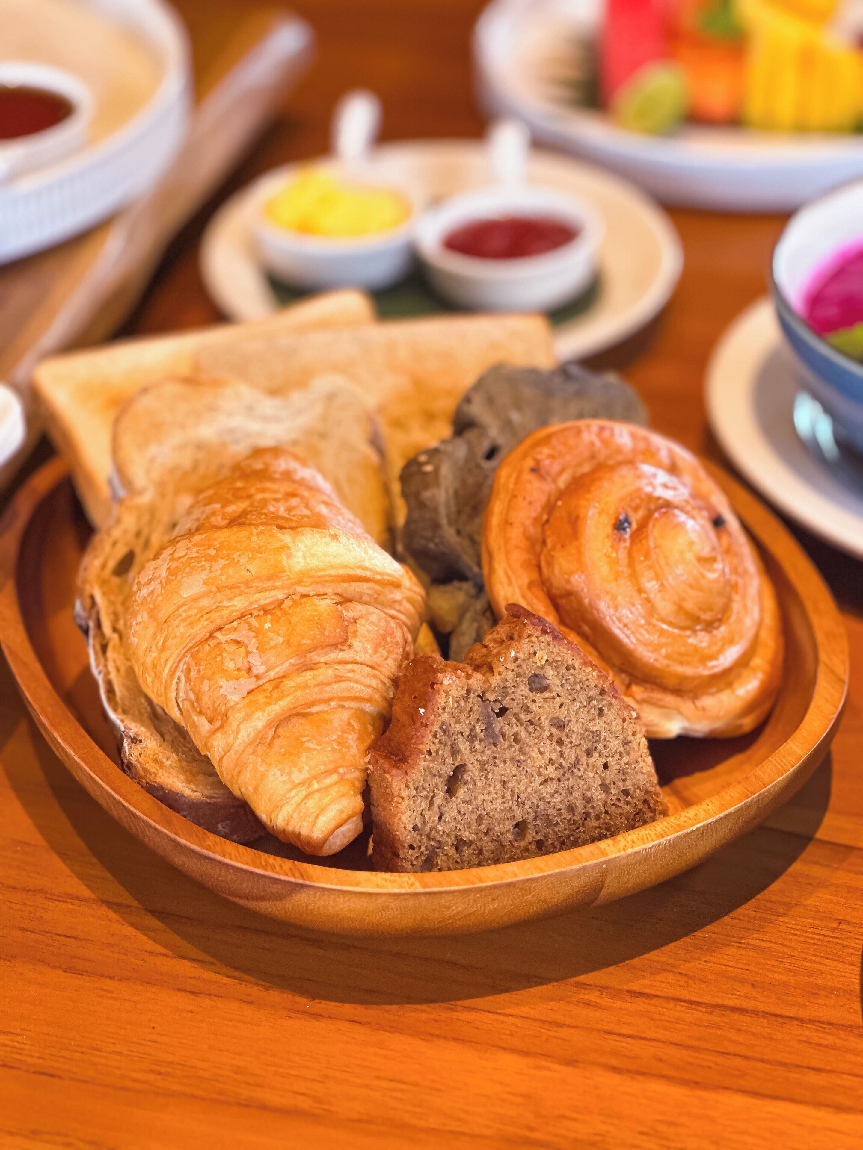 Una bandeja de madera con croissants y pan sobre una mesa.