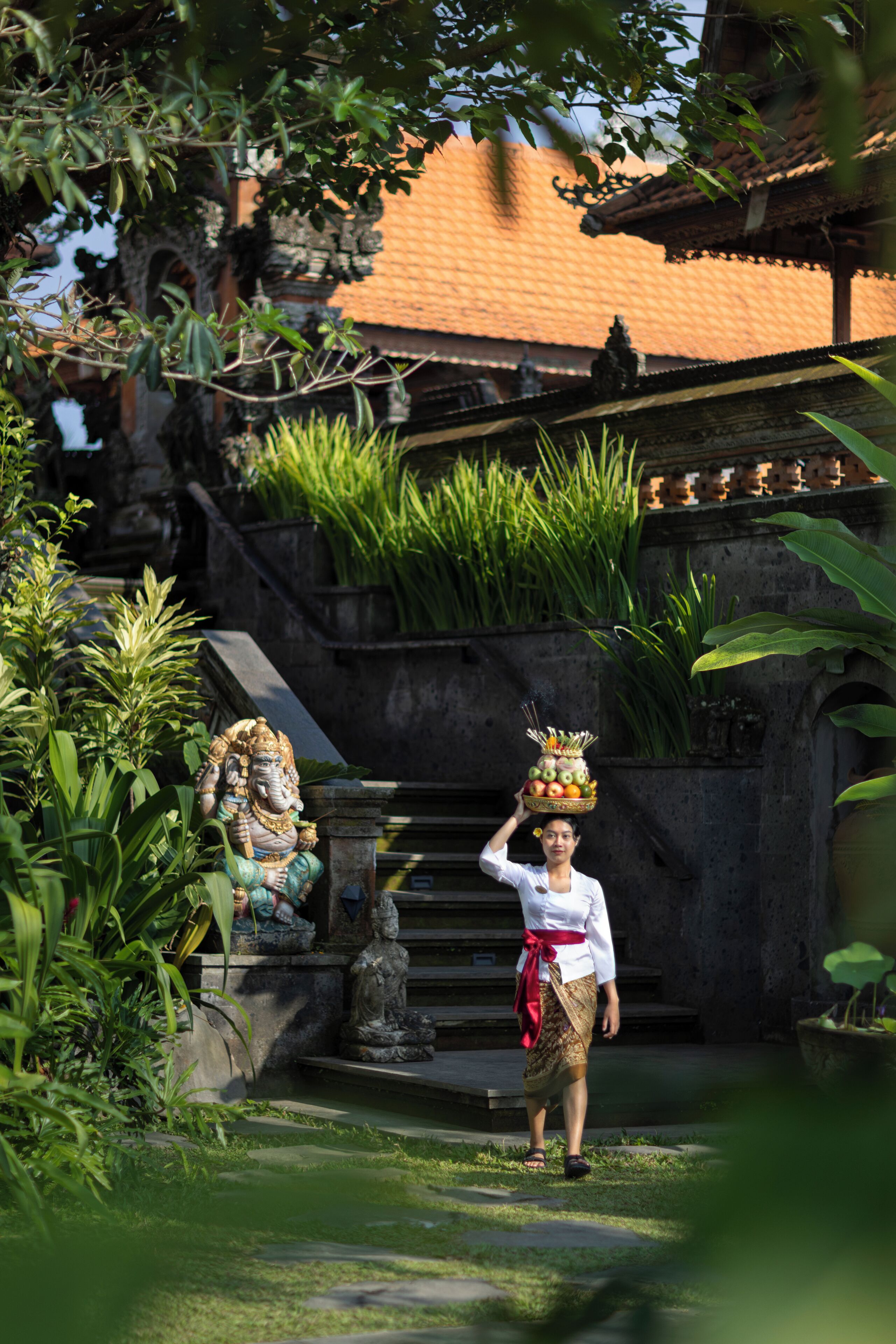 A person carrying a basket on their head, a statue, and a building with a tiled roof.