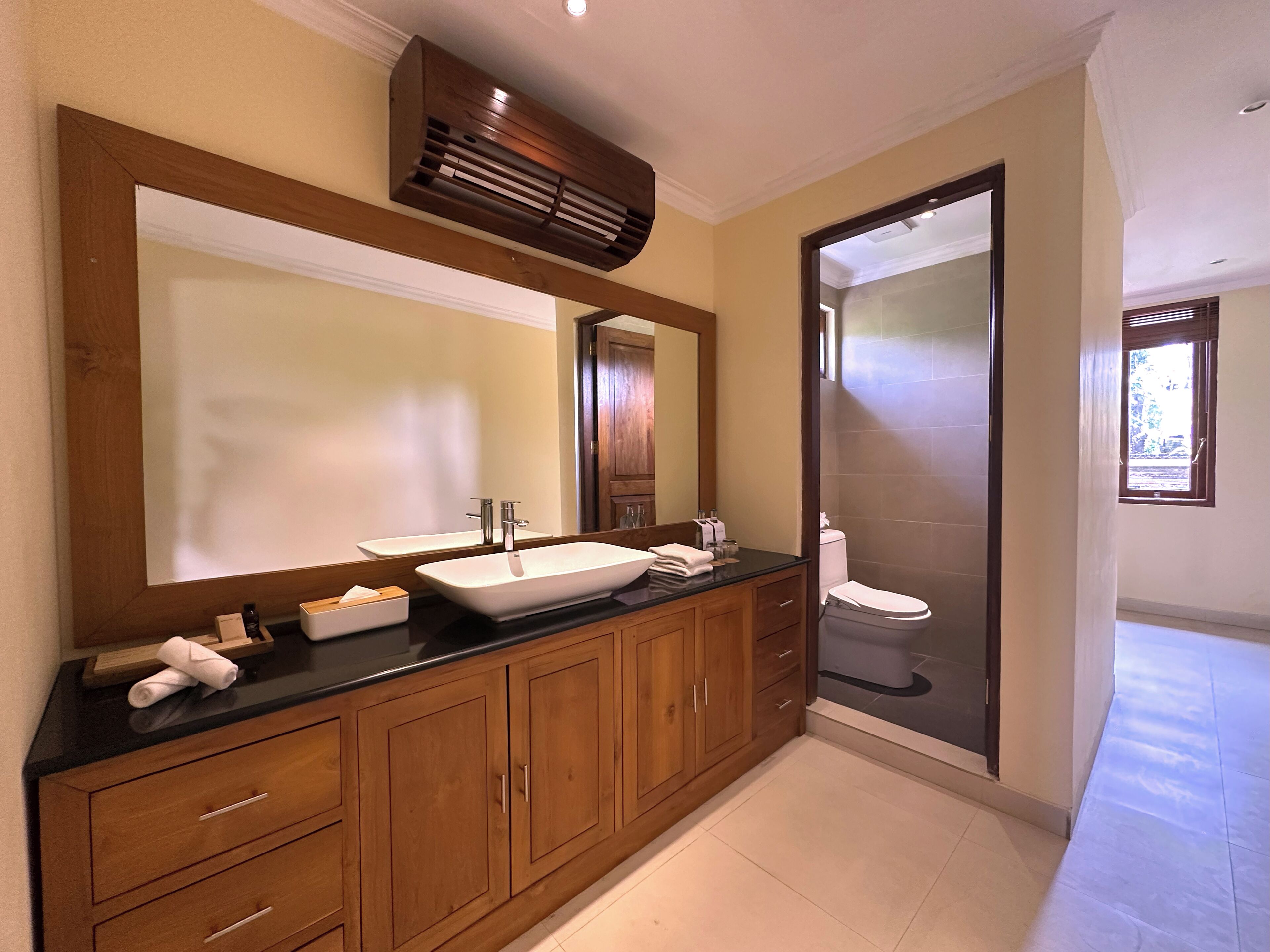 Un baño con un espejo grande, muebles de madera, encimera negra y cabina de ducha de vidrio.