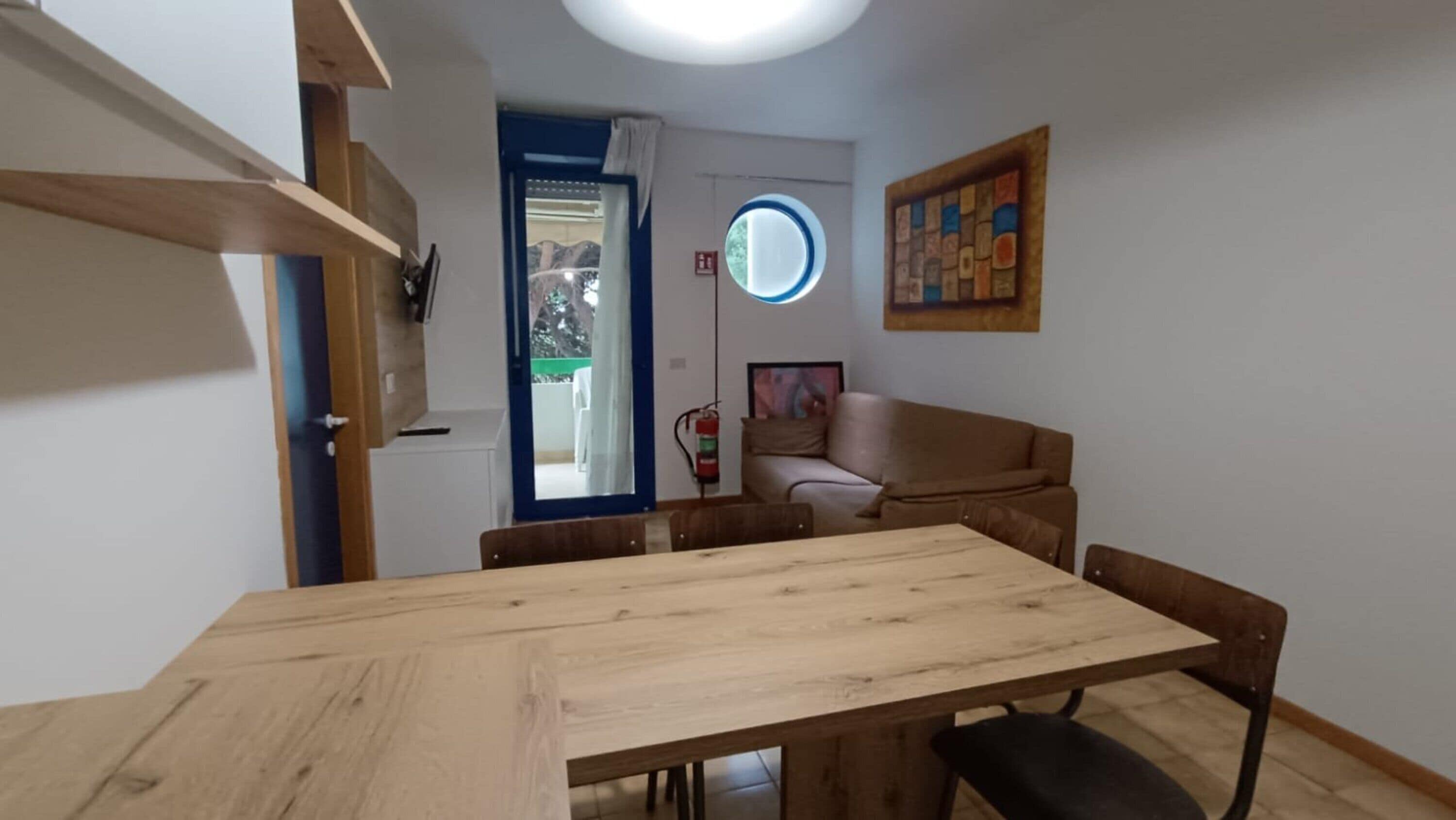 Un espacio habitable pequeño y funcional con una mesa de comedor, un sofá y un ventanal circular.