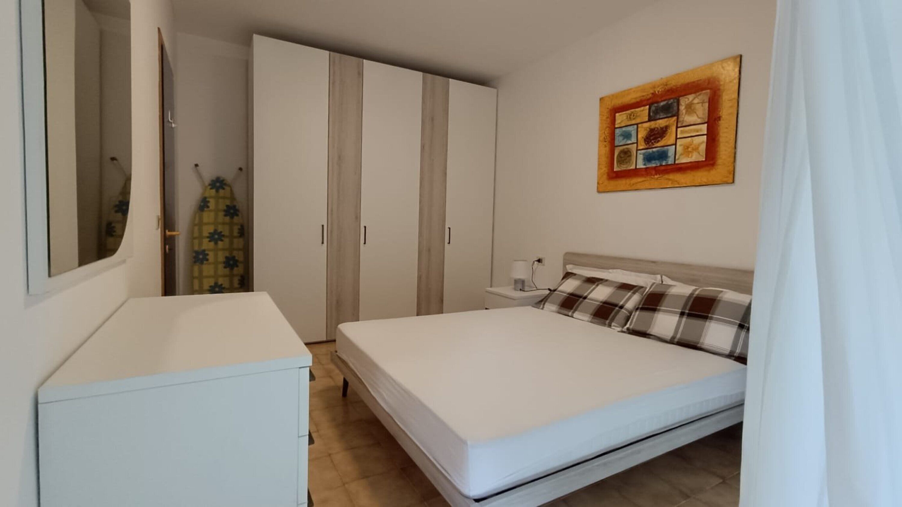 A bedroom with a bed, a bedside table, a wardrobe, and a painting on the wall.
