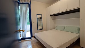 A bedroom with a bed, a wardrobe, a mirror, and a door with a curtain. - Seaside Escape for six Guests in Bibione (San Michele al Tagliamento)
