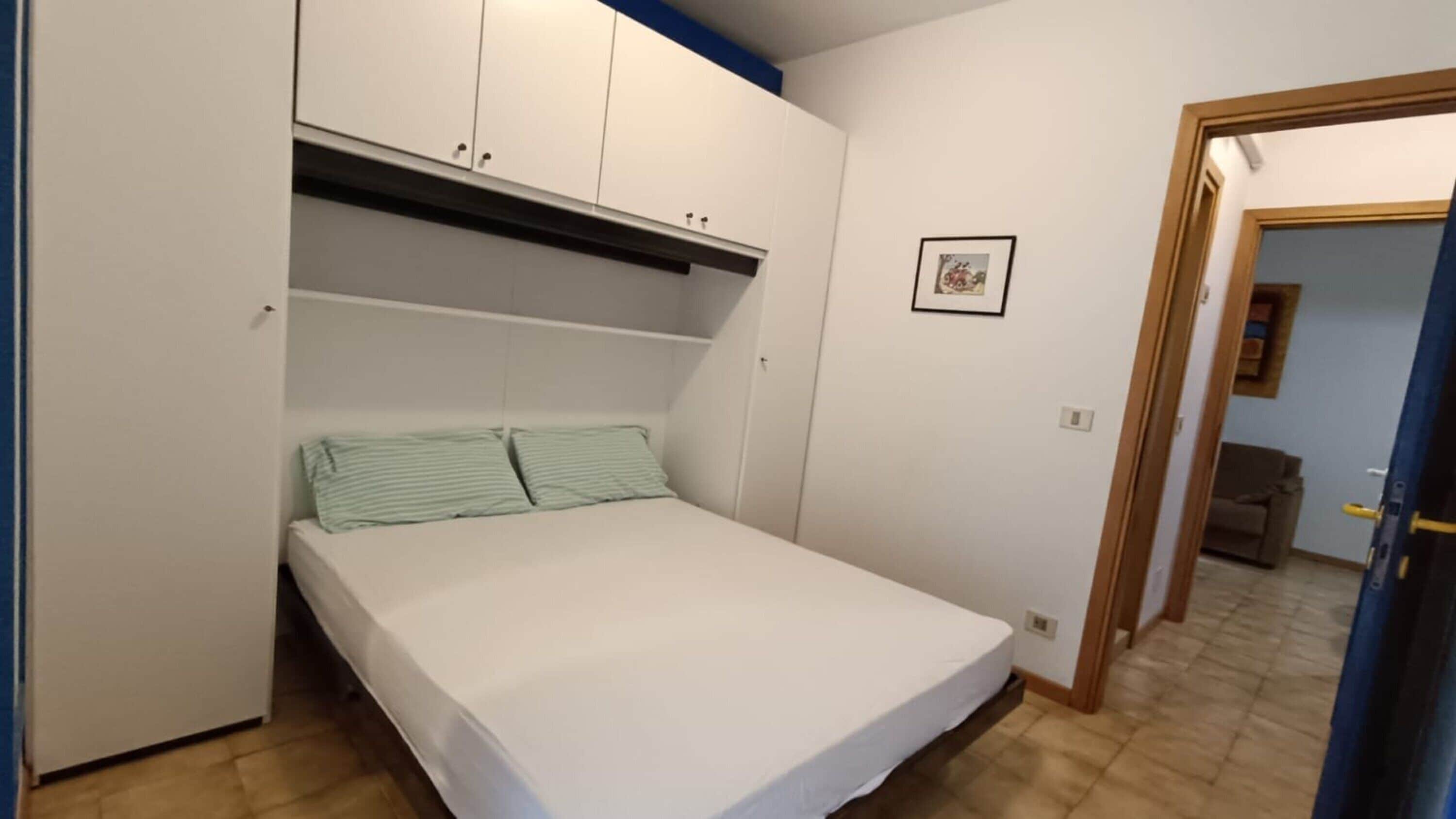 A bedroom with a bed, a wardrobe, and a door leading to another room.