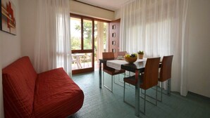 Um quarto com sofá vermelho, mesa de jantar com cadeiras e vista para área externa por uma porta de vidro.