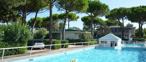 A swimming pool with a lifeguard tower, surrounded by trees and residential buildings.