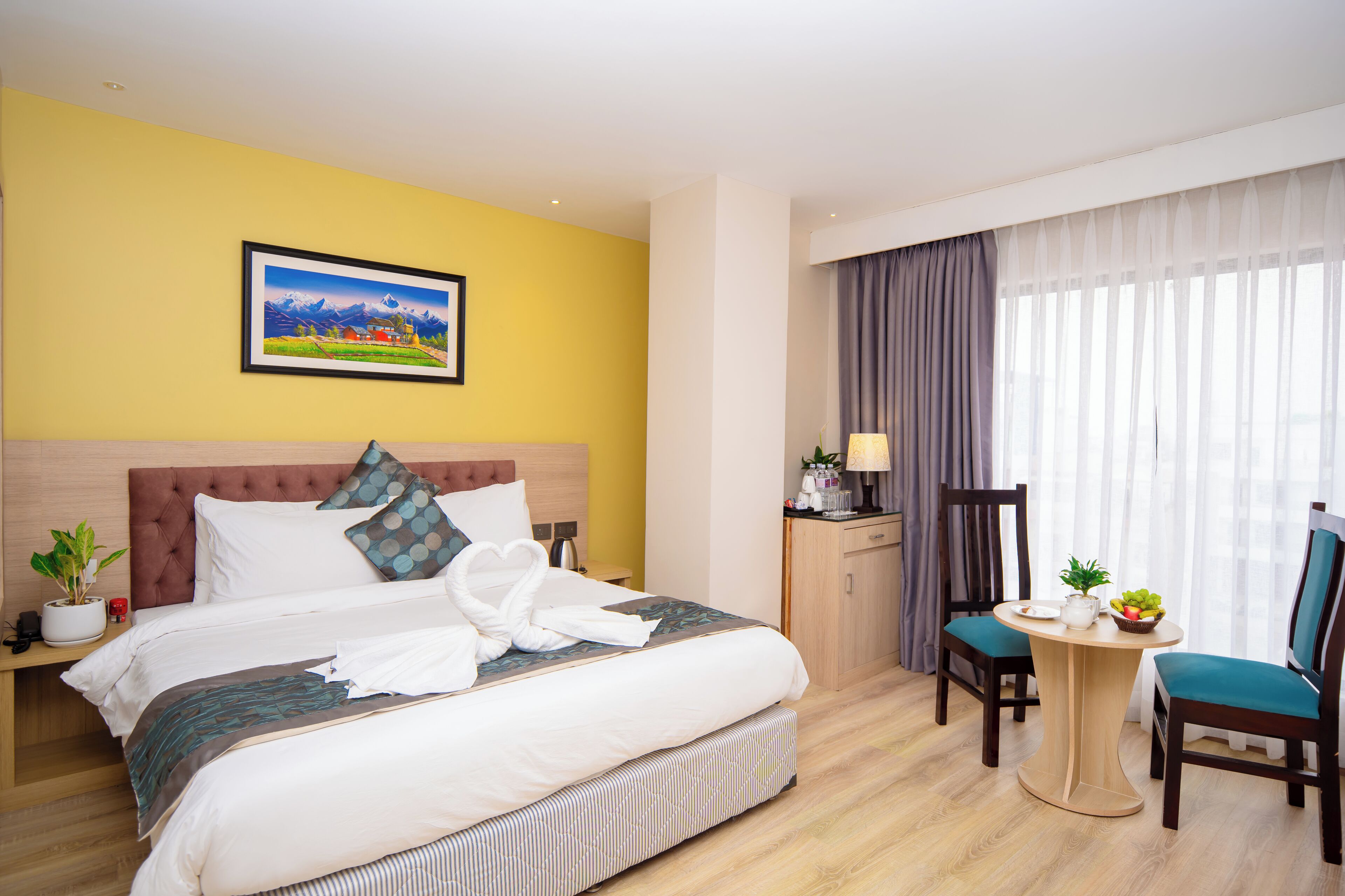A hotel room with a large bed, a desk with a chair, a potted plant, and a painting on the wall.