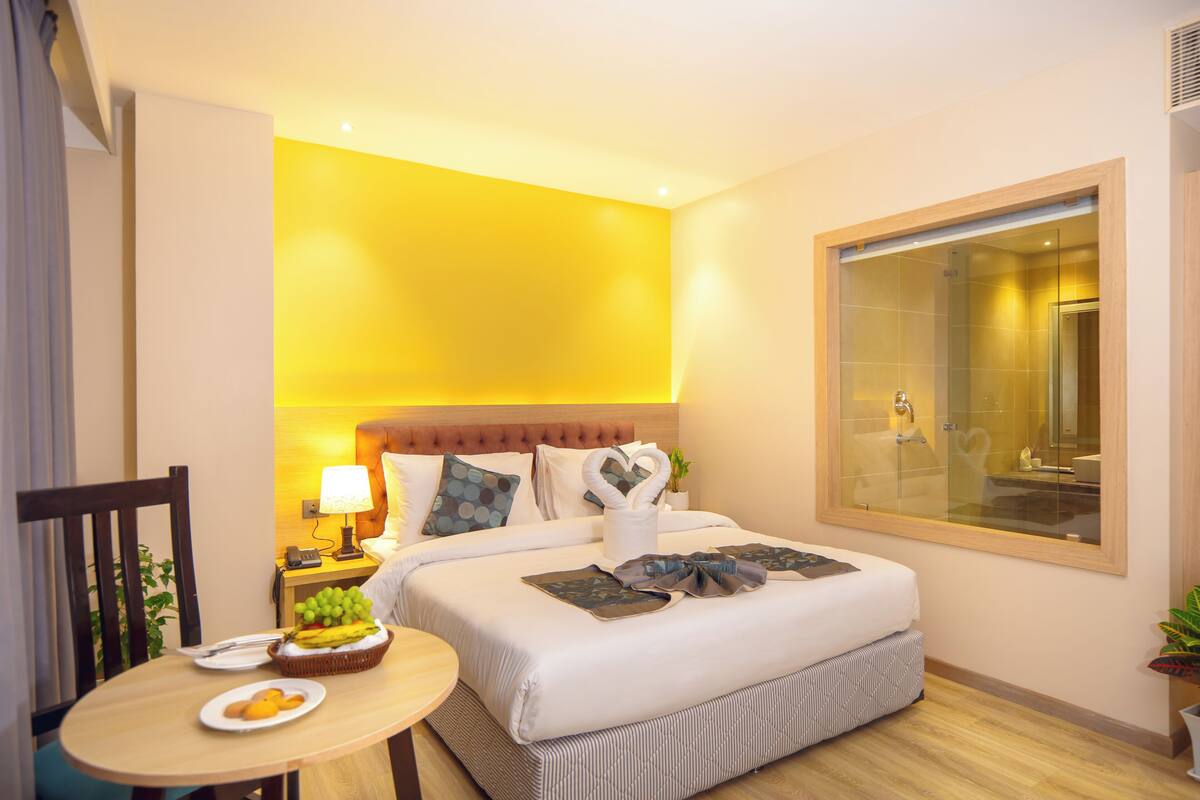 A hotel room with a bed, bedside table, lamp, and a large window.