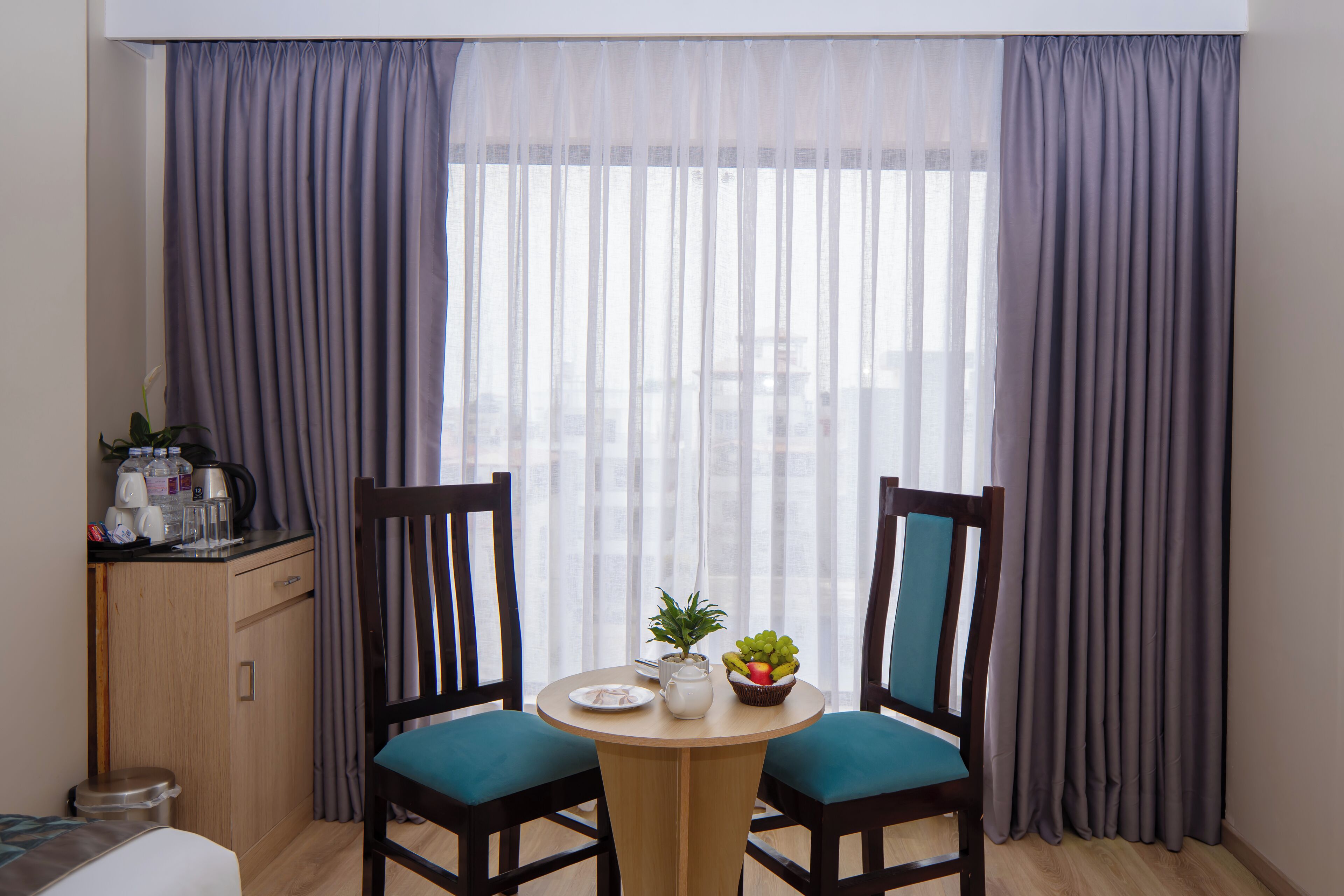 Una habitación con una mesa de comedor, dos sillas, un armario pequeño y una ventana con cortinas.