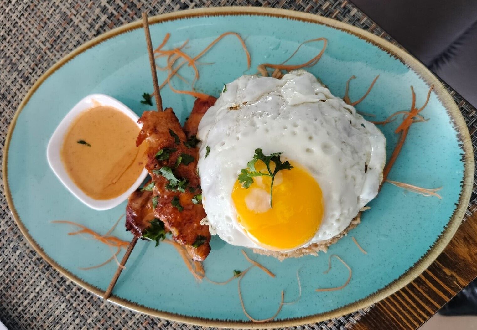 Une assiette avec un œuf au plat, du bacon et un petit bol de sauce.