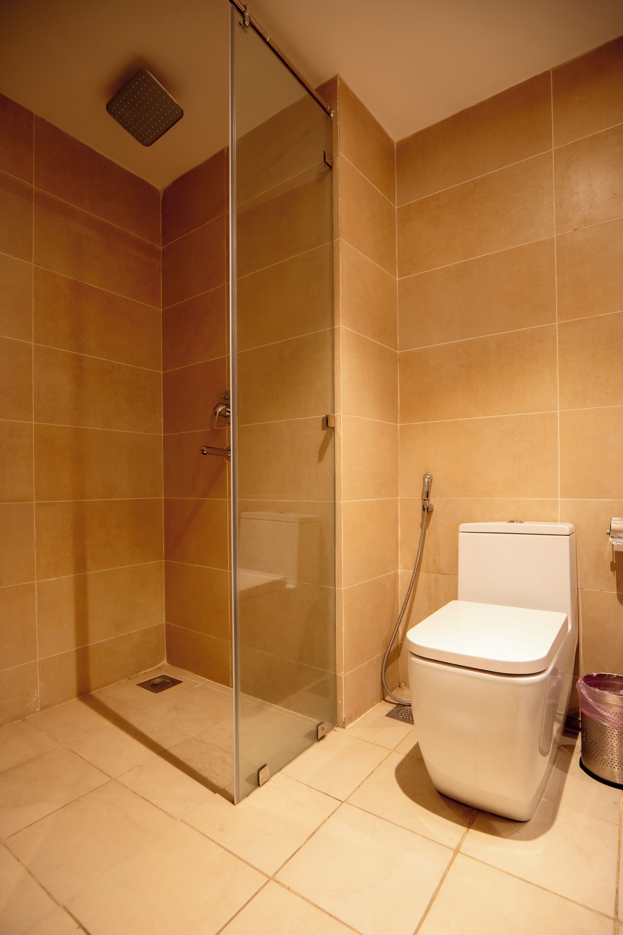 A bathroom with a glass shower enclosure, a toilet, and a trash bin.