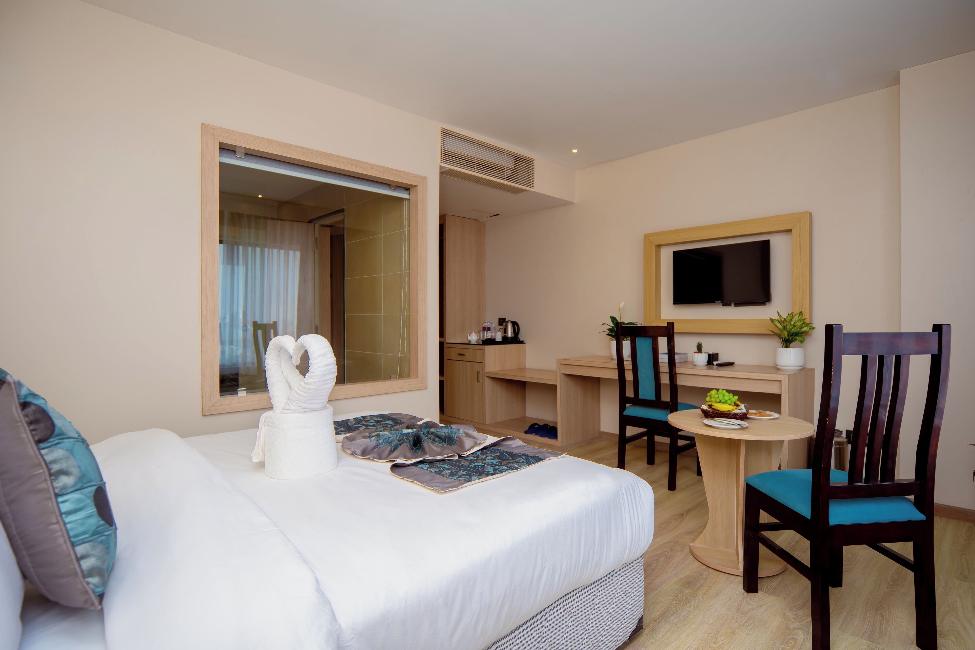 Una camera d'albergo con un letto, una scrivania, una sedia, una TV e un piccolo tavolino con una pianta.