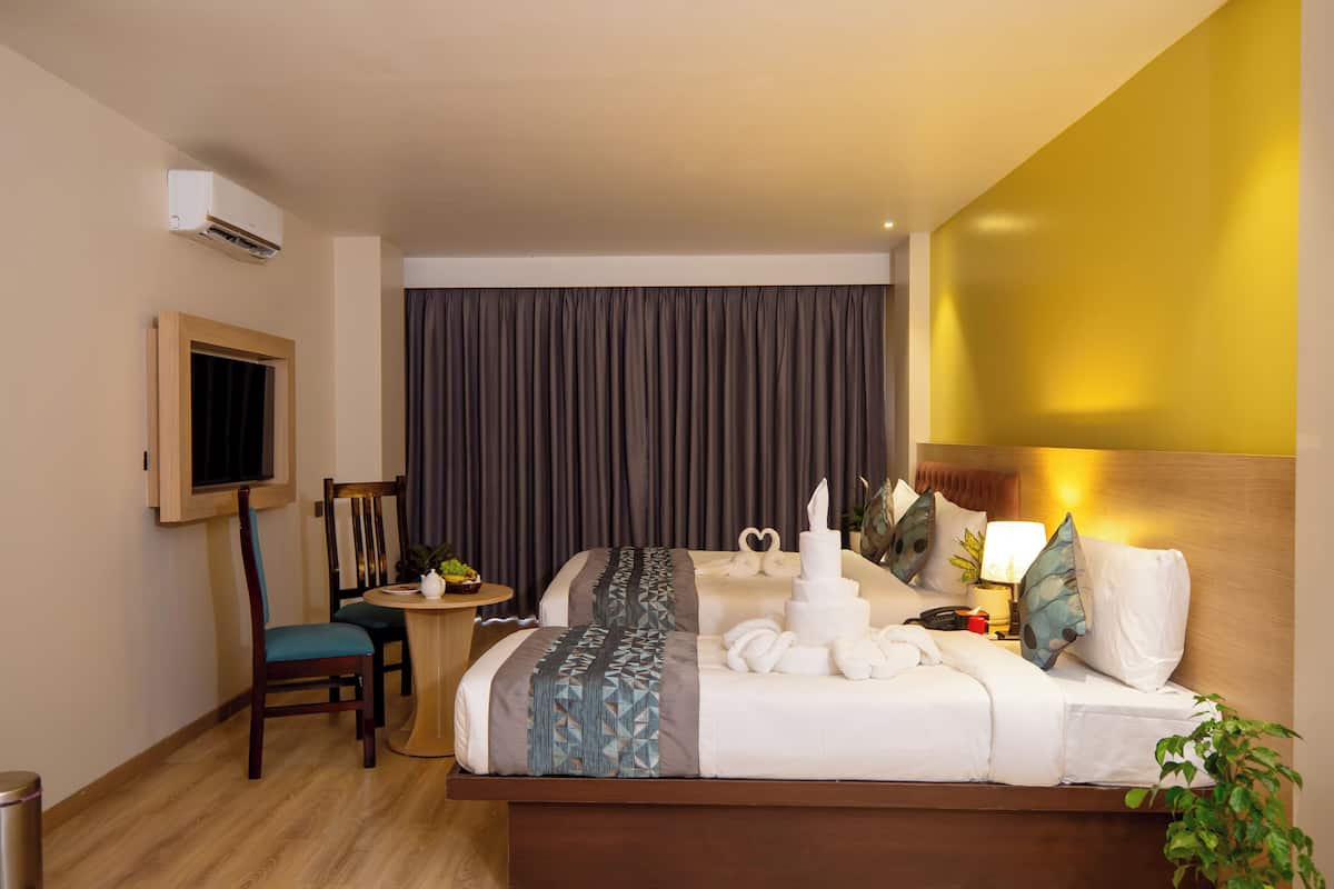 A hotel room with a bed, bedside table, lamp, and a TV mounted on the wall.