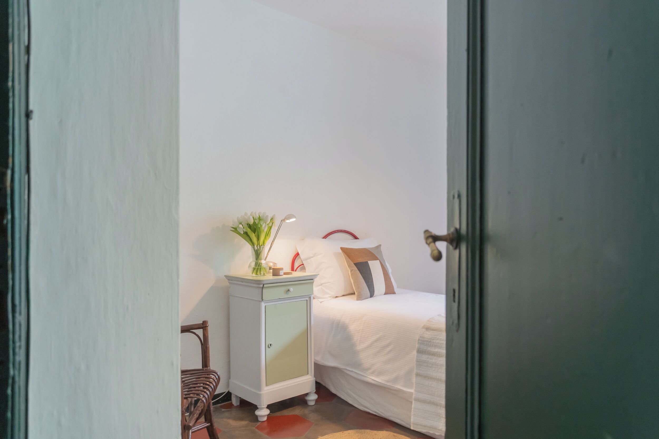 A bedroom with a bed, a nightstand, a lamp, and a chair.