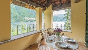 A balcony with a table set for dining, overlooking a lake and mountains. - Residenza Regina by Rent all Como (Laglio)