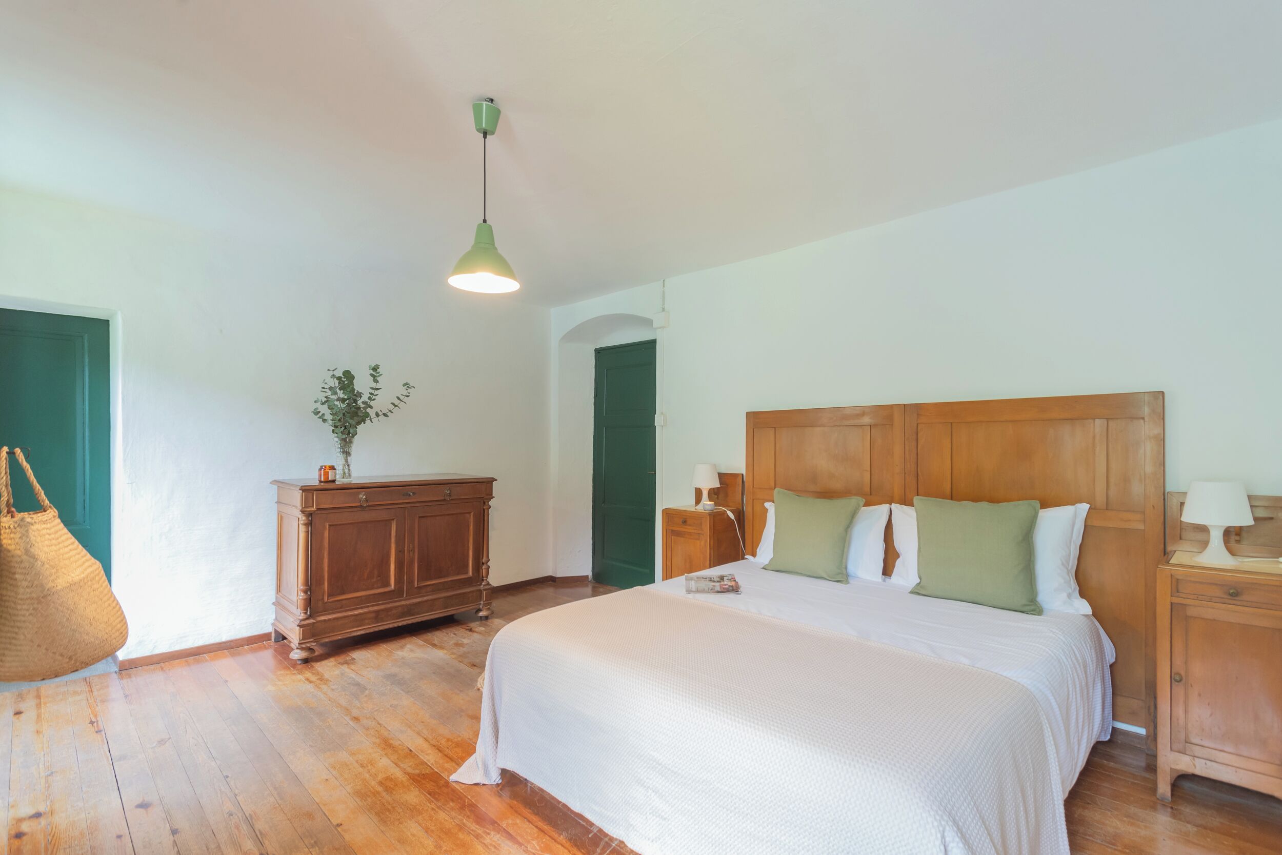 A bedroom with a wooden bed, a nightstand, a dresser, and a hanging lamp.