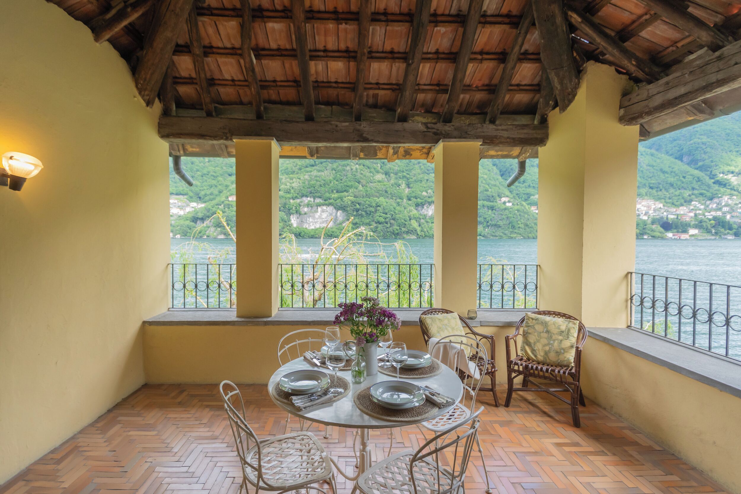 Un coin repas avec une table dressée pour quatre personnes, offrant une vue imprenable sur un lac et des montagnes.