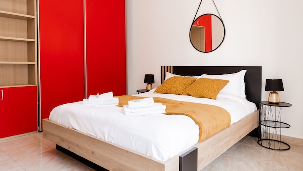 A modern bedroom with a wooden bed, red wardrobe, and a round mirror on the wall.