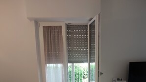 Et værelse med en skydedør til en balkon, et lille bord med en stol og et fladskærms TV på et stativ.