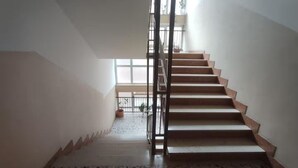 En trappe med gelænder i metal fører op til en balkon. Gulvet er flisebelagt med et stribet mønster.