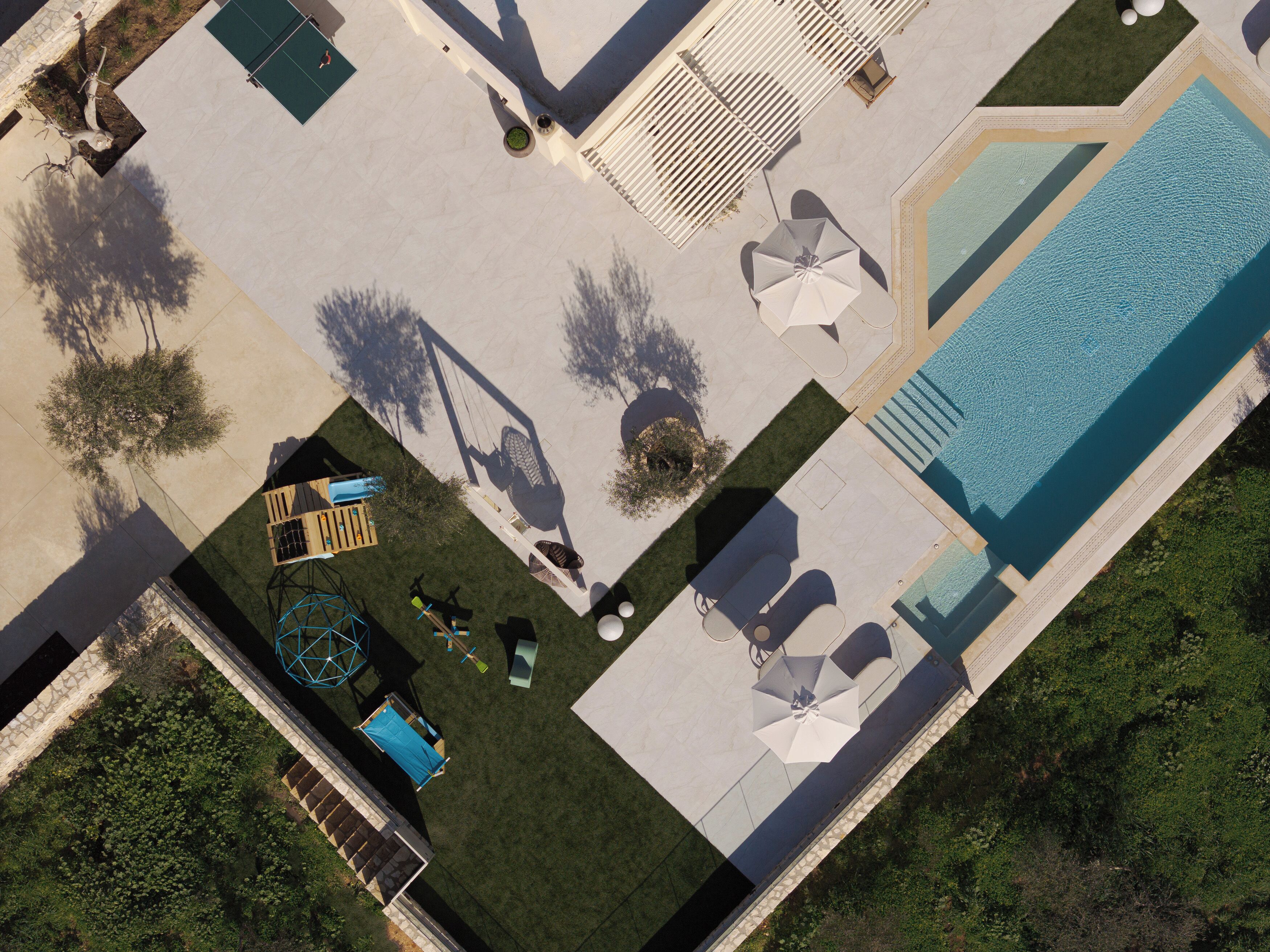 An aerial view of a resort with a swimming pool, sun loungers, and a children's play area.