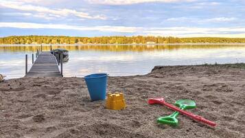 Une plage de sable avec une jetée en bois qui s’avance sur un lac paisible, le tout entouré d’arbres.