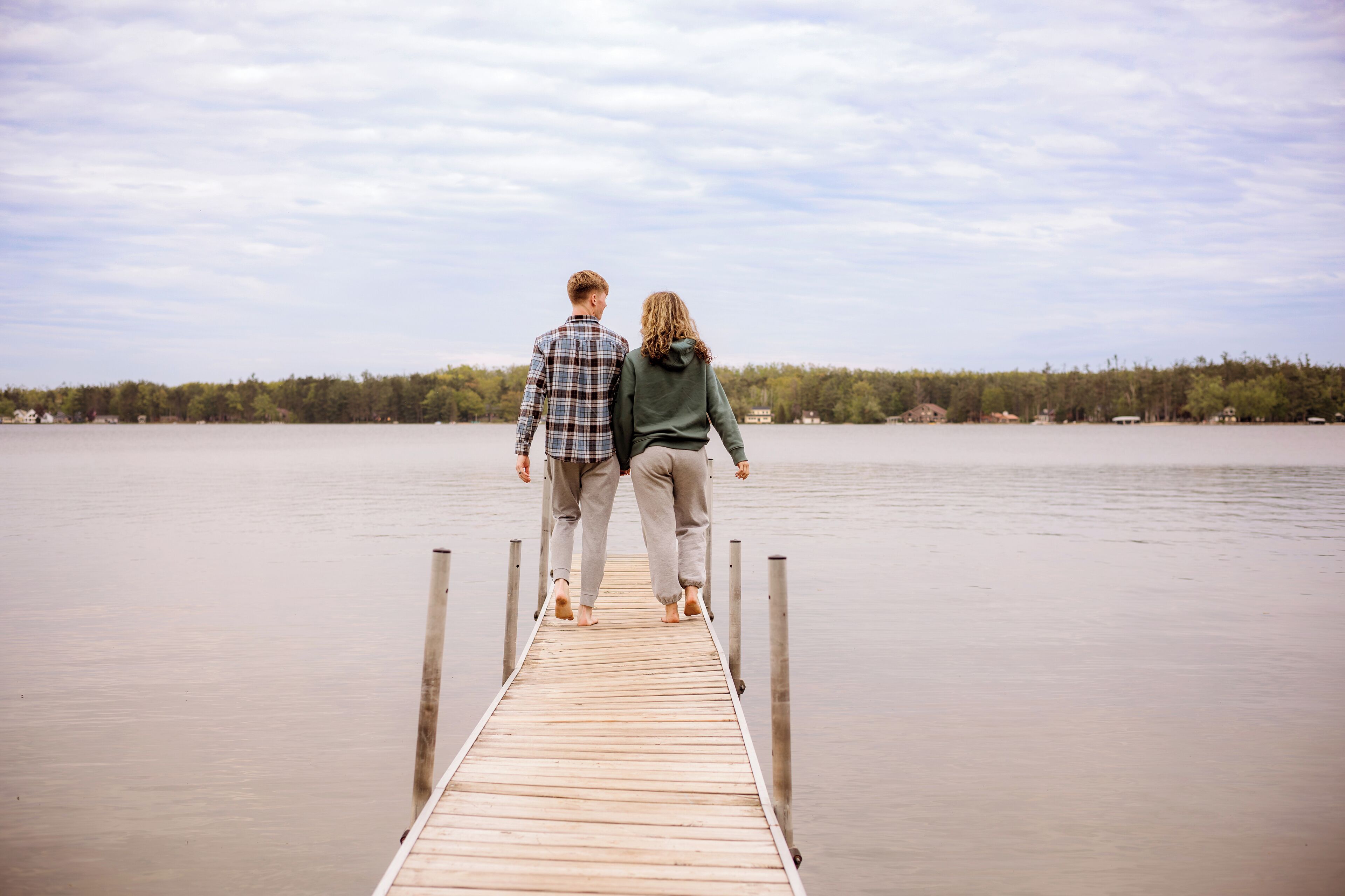 A wooden pier extending into a calm lake with a forested shoreline in the background.