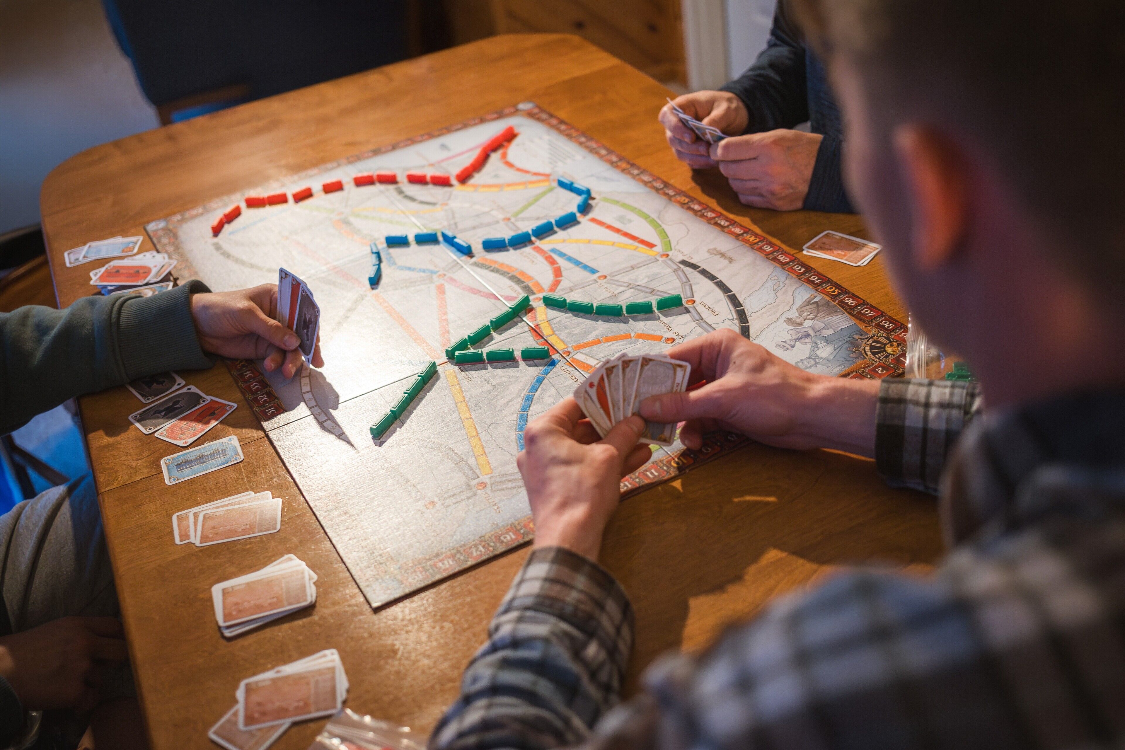 A group of people playing a board game at a wooden table.