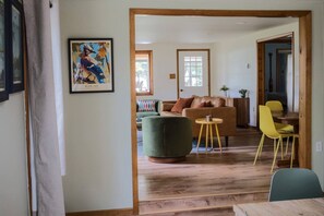 A living room with a sofa, a green armchair, a wooden coffee table, and yellow chairs.