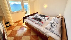 A bedroom with a bed, a nightstand, a lamp, a window with a view of the sea, and a ceiling light. - Studio Apartman Mare 2 (Dramalj)