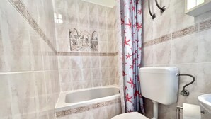 A bathroom with a bathtub, toilet, and shower curtain. - Studio Apartman Mare 2 (Dramalj)