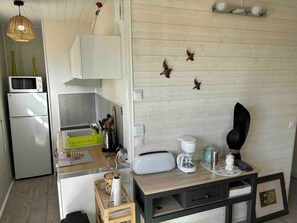 Une cuisine compacte équipée d’un four à micro-ondes, d’un réfrigérateur et d’une machine à café posée sur le plan de travail.