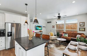 Une cuisine moderne avec des meubles blancs, un réfrigérateur en acier inoxydable et un coin repas comprenant un canapé marron et une table basse.
