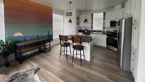 A modern kitchen with white cabinets, a central island, bar stools, and a dining area with a bench and chairs. - Disney SoFi Stadium Hollywood Beaches Close! Central AC (Norwalk)