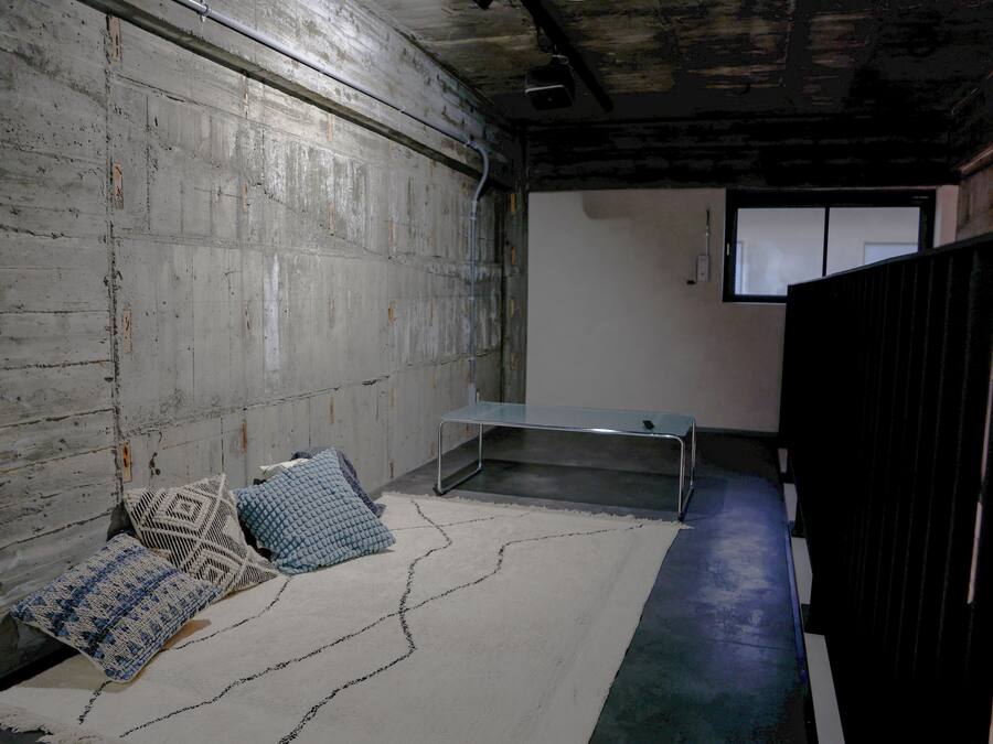 Ein Zimmer mit einer Betonwand, einer Metallbank und gemusterten Kissen.