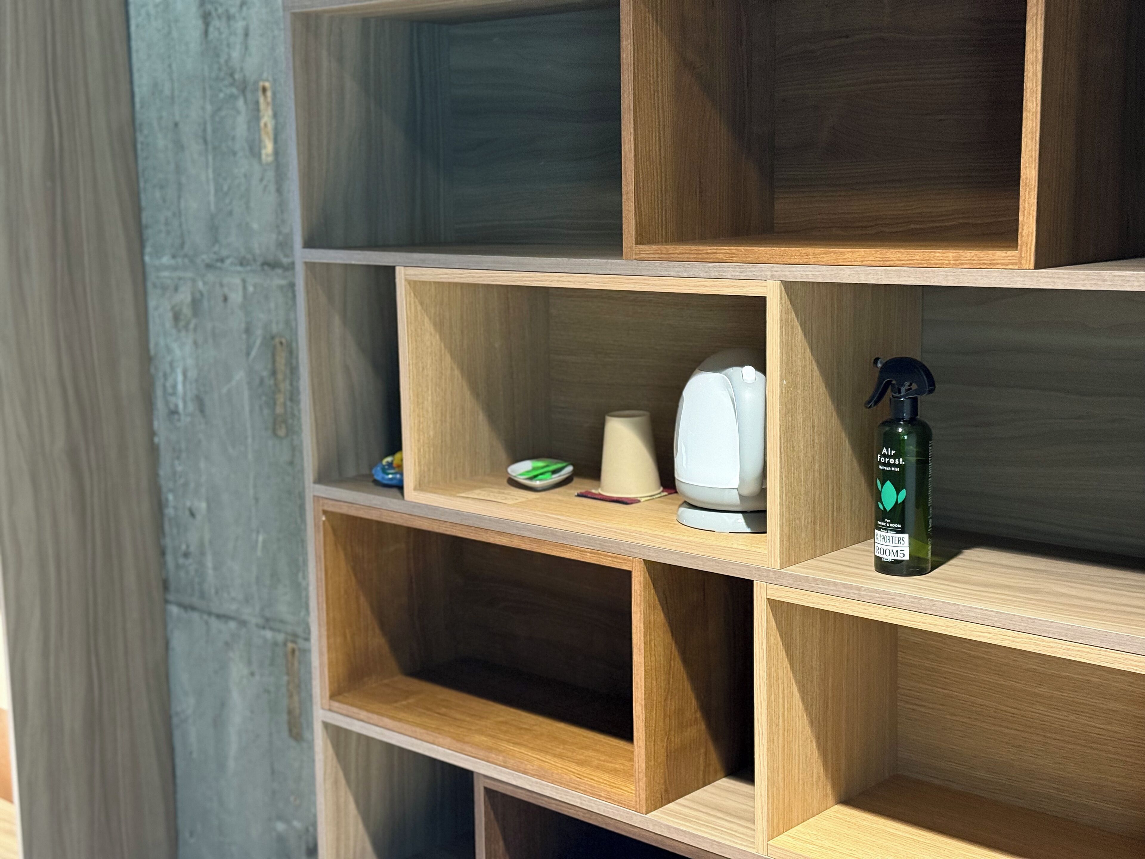 A wooden shelf unit with multiple compartments, some containing items like a white object, a green object, and a spray bottle labeled "Air Forest."