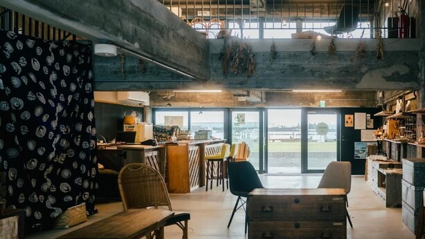An open-plan bar area with a high ceiling, exposed ductwork, and a view through large windows. - Re PORT HOTEL (Yaizu)