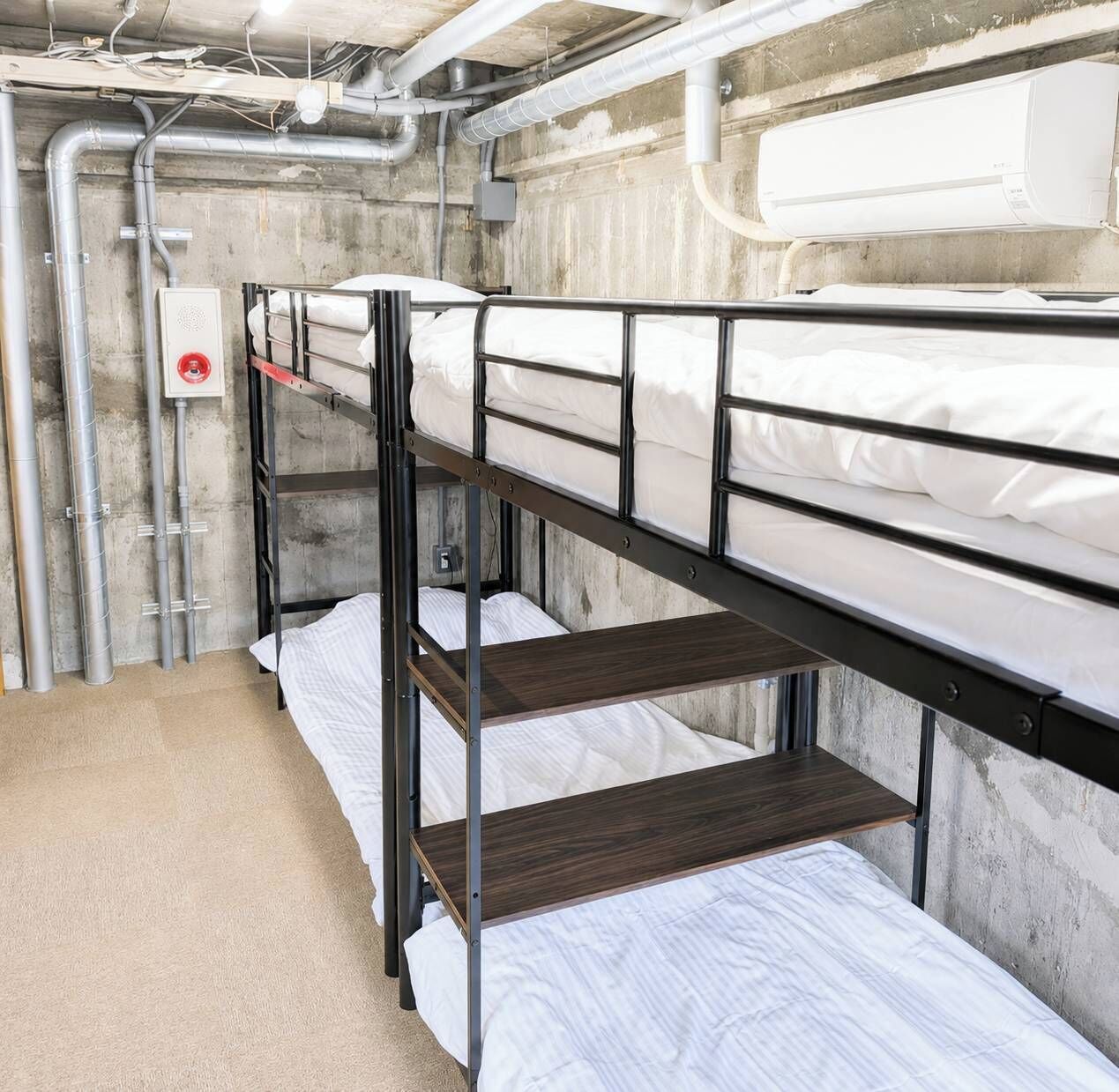 A bunk bed room with metal railings, white bedding, and visible pipes on the walls.