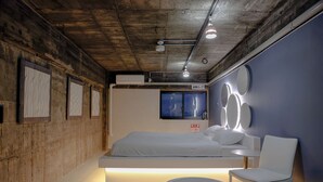 A modern hotel room with a large bed, a seating area with a round table, and a wall with circular light fixtures. - Re PORT HOTEL (Yaizu)