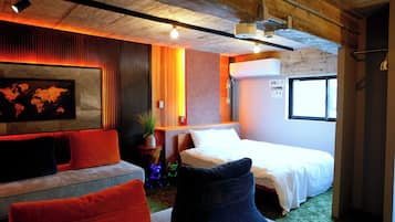 A hotel room with a bed, a sofa, a small table, a potted plant, and a world map on the wall.