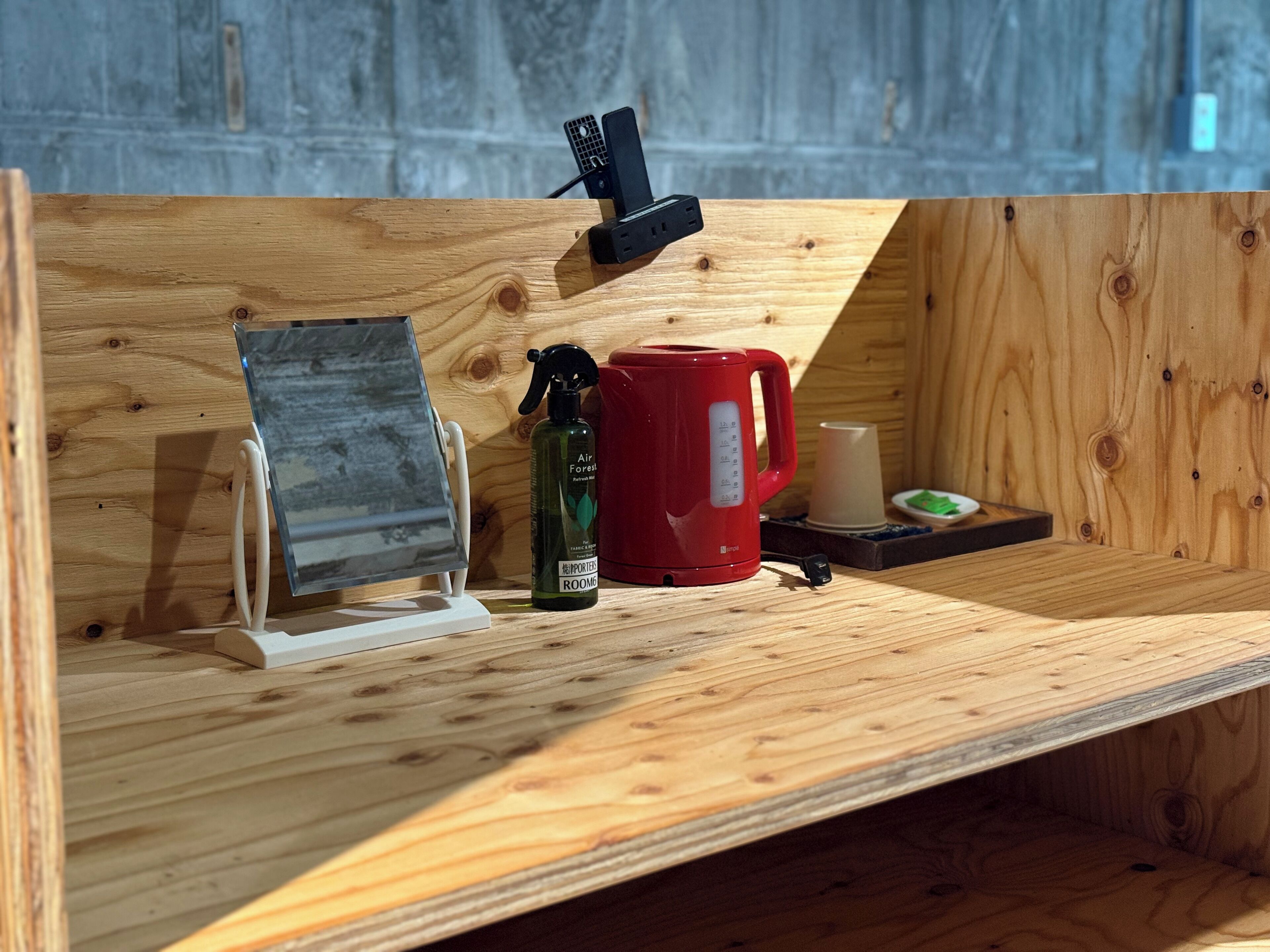A wooden shelf with a red mug, a spray bottle, and a white cup.