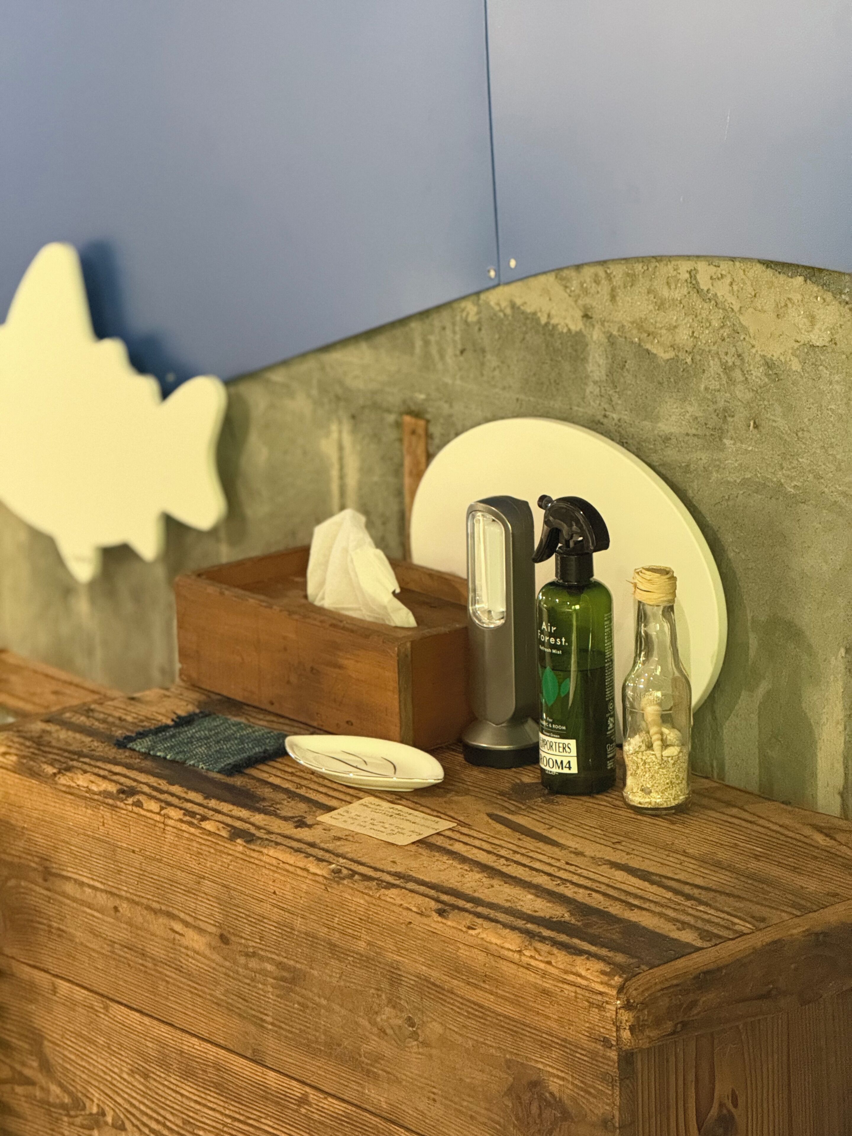 Una encimera de madera con una caja de pañuelos, un pulverizador, una botella de vidrio y un plato.