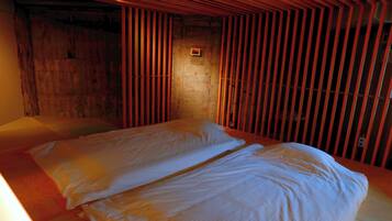 A room with a wooden slatted wall, a bed with white bedding, and a small window.