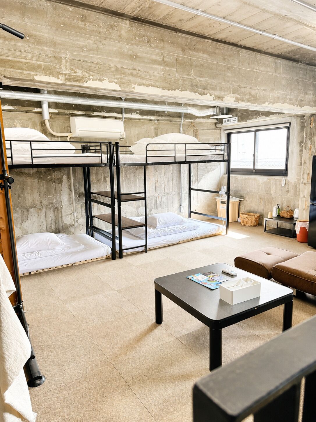 A dormitory room with bunk beds, a table, and a window.