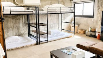 A dormitory room with bunk beds, a table, and a window.