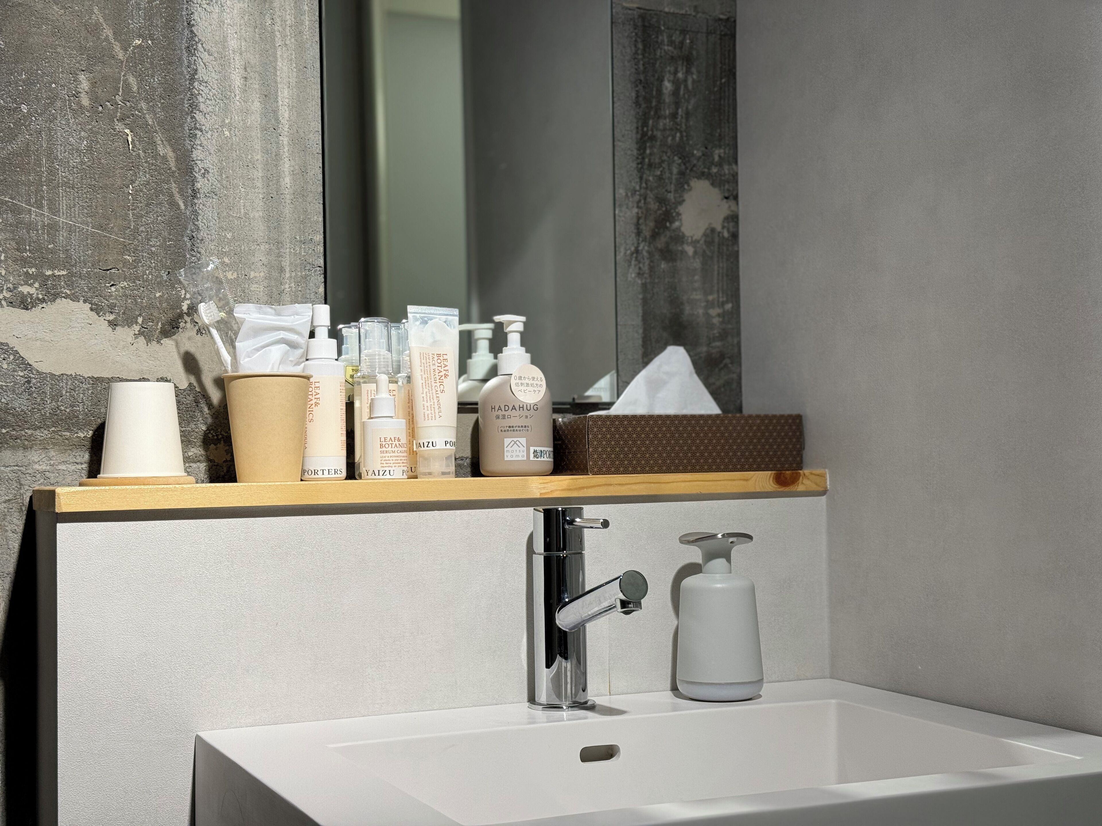 Un baño con lavamanos blanco, un espejo y una repisa con diversos artículos de tocador.