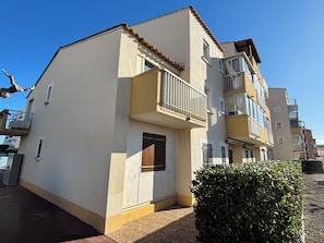 A multi-story residential building with balconies, a small entrance door, and a hedge in front. - Bright village apartment with terrace and parking 50m from the sea (Le Barcarès)