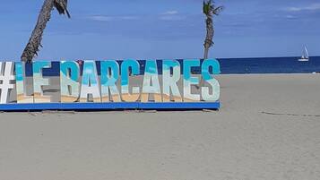 Un cartel de playa con el texto '#LE BARCARES' y palmeras al fondo.