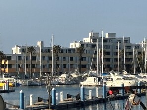 A marina with boats docked, a clear sky, and a multi-story building in the background.