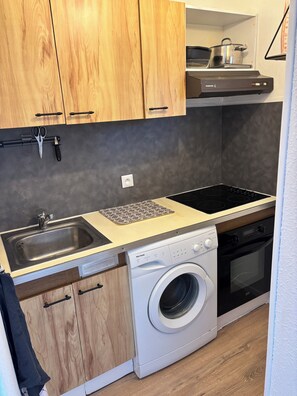 A compact kitchen with wooden cabinets, a sink, a built-in oven, and a washing machine.